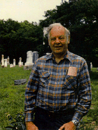 Photograph of Homer White; casual flannel shirt, strong rectangular face with pleasant features, an engaging smile, and shock of white hair.