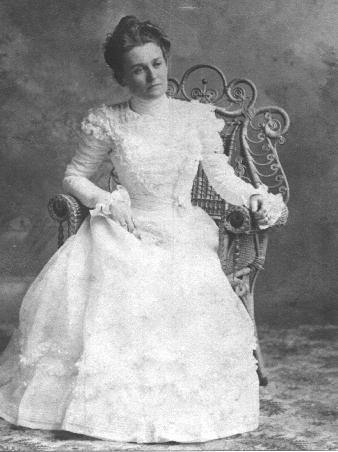Daisy Tedrow as a young woman, seated in a wrought-wicker chair in a beautiful white ruffled dress.